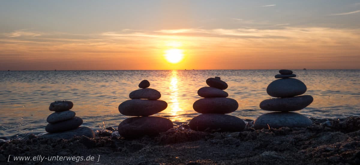 Sonnenuntergang auf Fehmarn mit Steintürmchen am Strand